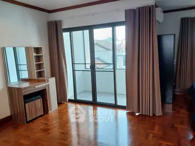 Spacious bedroom with large windows and balcony access, featuring wooden flooring and modern furnishings.