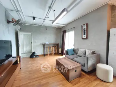 Modern living room with industrial design, featuring wooden flooring, cozy sofa, and stylish lighting.