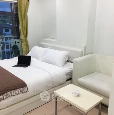 Modern bedroom with cozy white bed, laptop, and elegant armchair near window with city view.