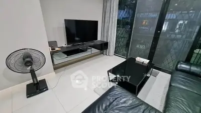 Modern living room with sleek black furniture and large TV, featuring floor-to-ceiling windows for natural light.