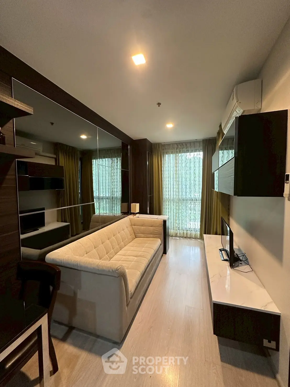 Modern living room with stylish decor, large mirror, and natural light from balcony.