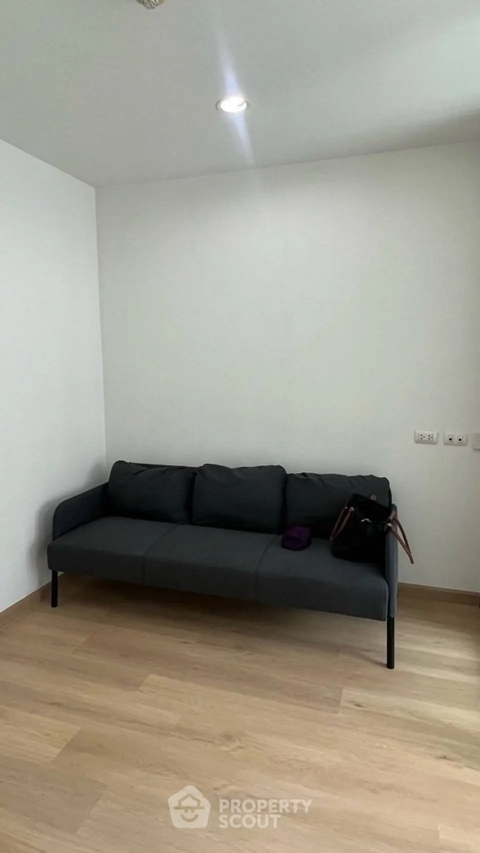 Minimalist living room with sleek black sofa and wooden flooring, perfect for modern urban living.