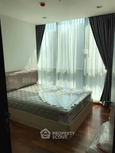 Modern bedroom with large window and elegant curtains, featuring a comfortable bed and wooden flooring.