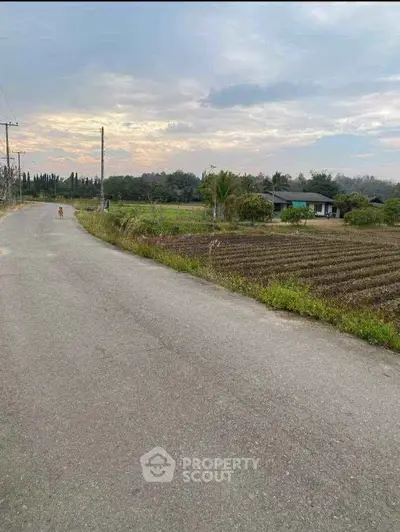 Scenic rural landscape with open fields and a distant house under a cloudy sky.