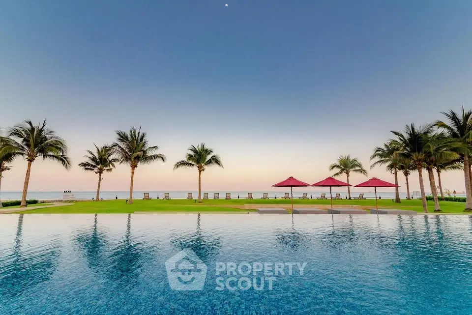 Stunning beachfront pool with palm trees and ocean view at sunset.
