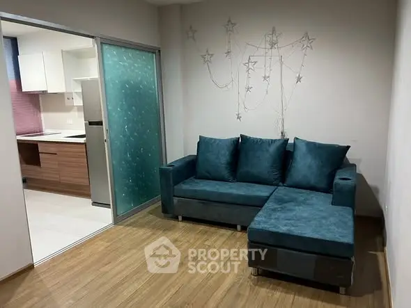 Modern living room with teal sofa and open kitchen layout, featuring stylish decor and wooden flooring.
