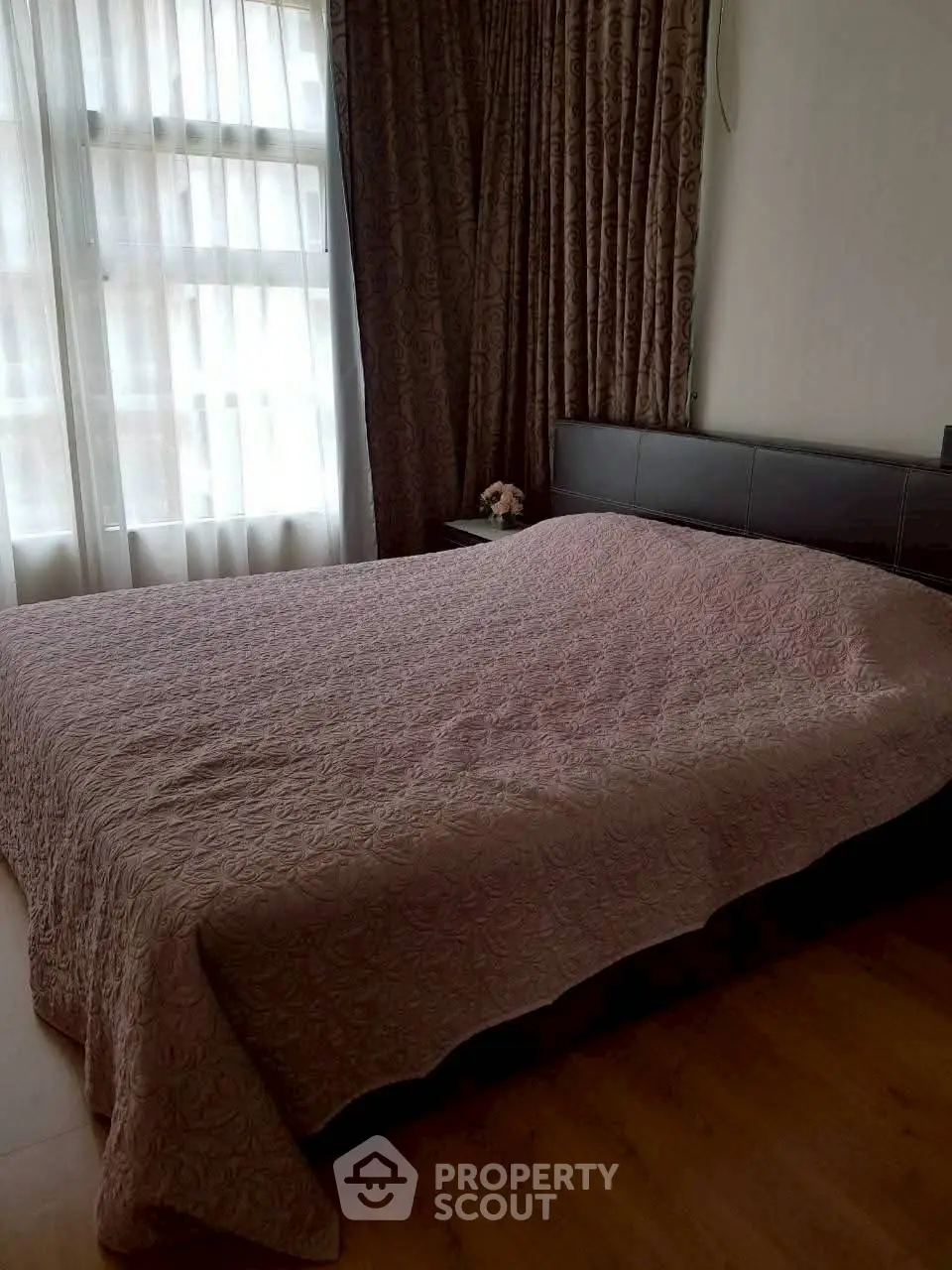 Cozy bedroom with large window and elegant curtains, featuring a comfortable bed and wooden flooring.