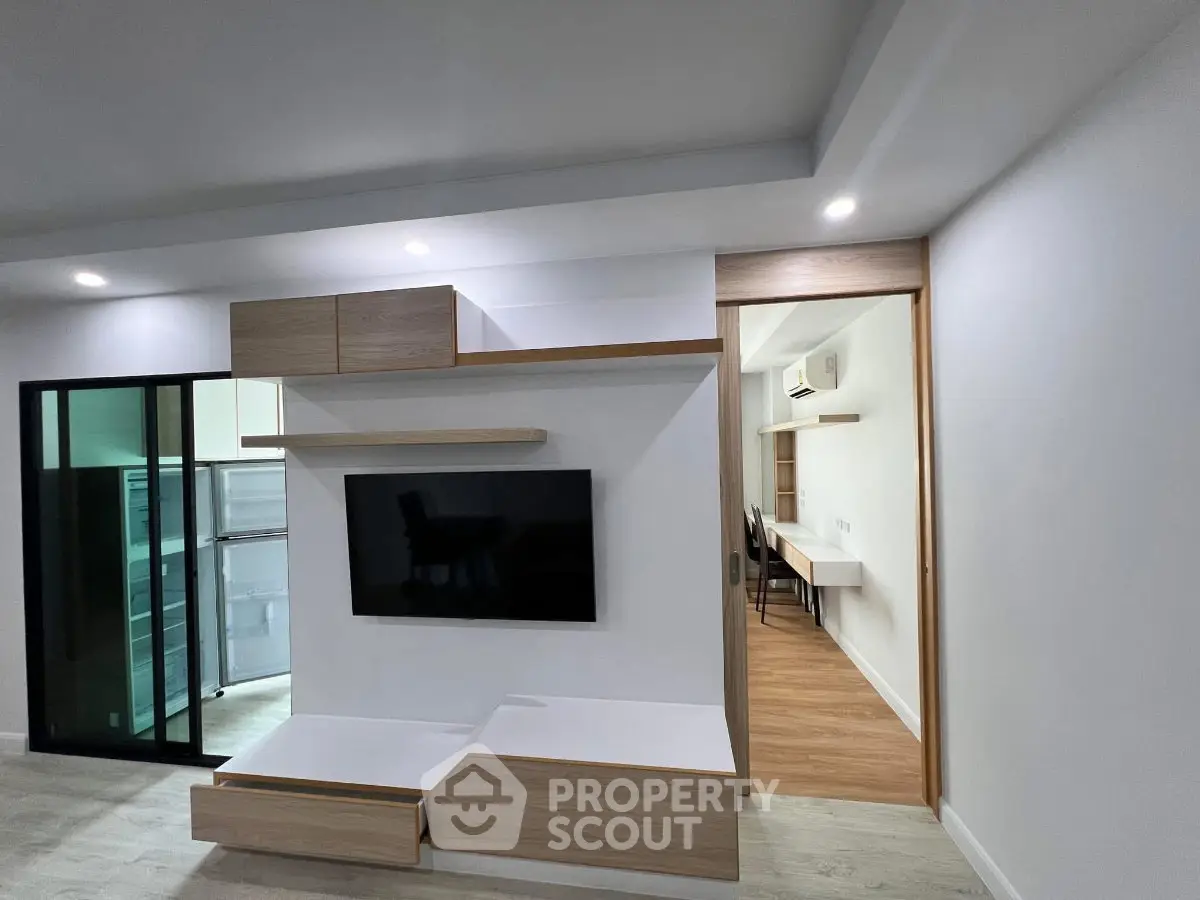 Modern living room with sleek TV unit and sliding door leading to dining area.