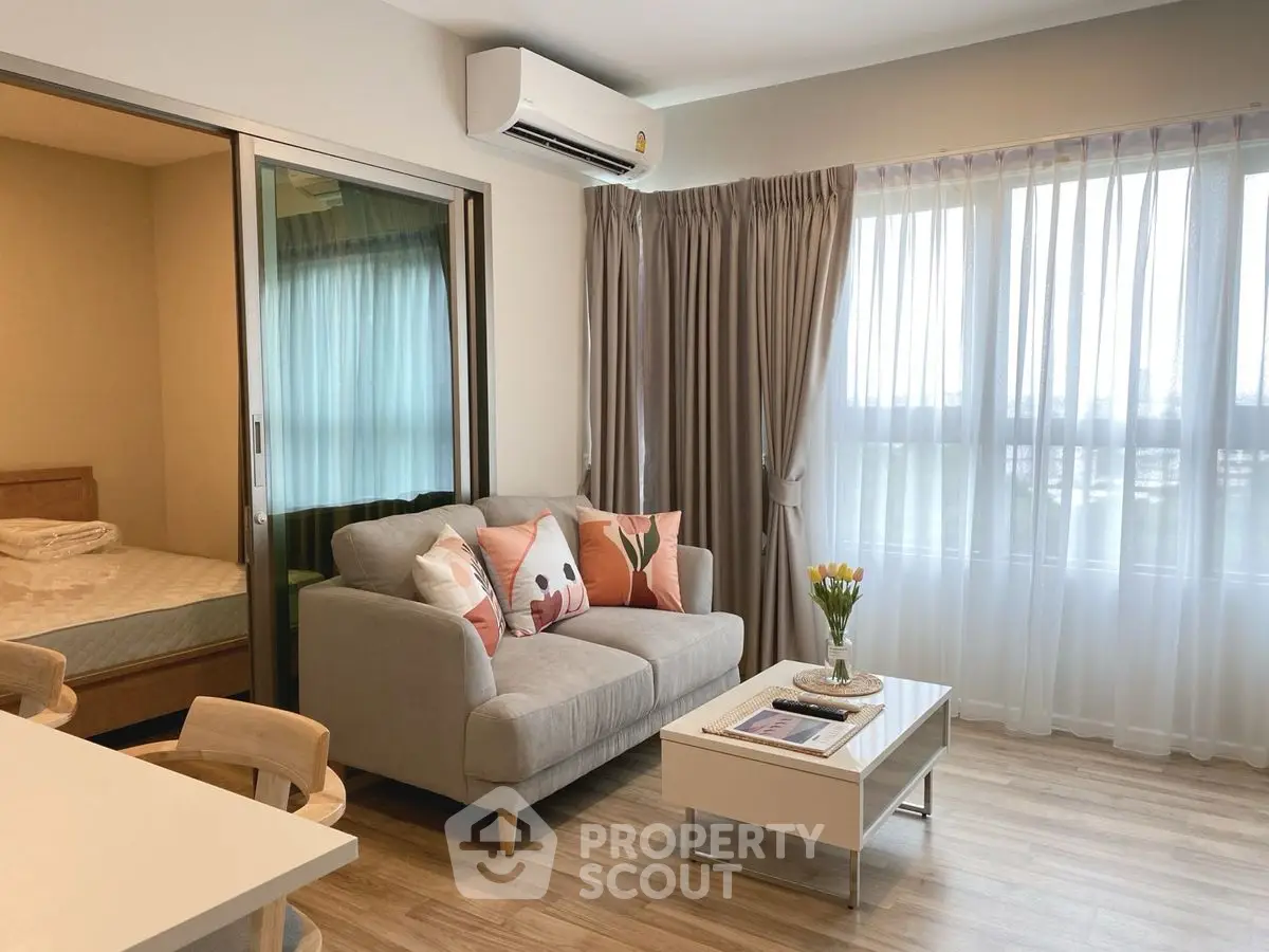 Modern living room with cozy sofa and natural light, adjacent to bedroom in open layout apartment.