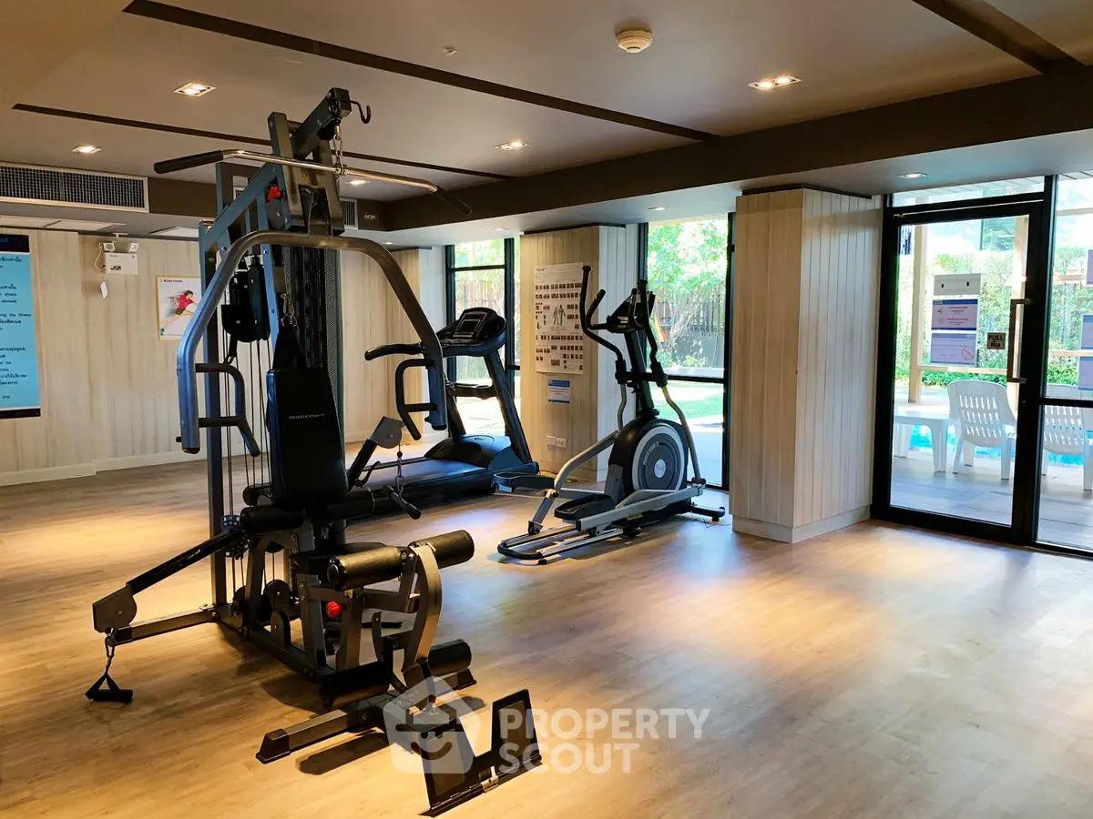 Modern gym with exercise equipment and pool view in luxury apartment complex.