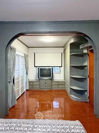 Spacious living room with vintage TV and built-in shelves, featuring elegant archway and polished wooden floors.