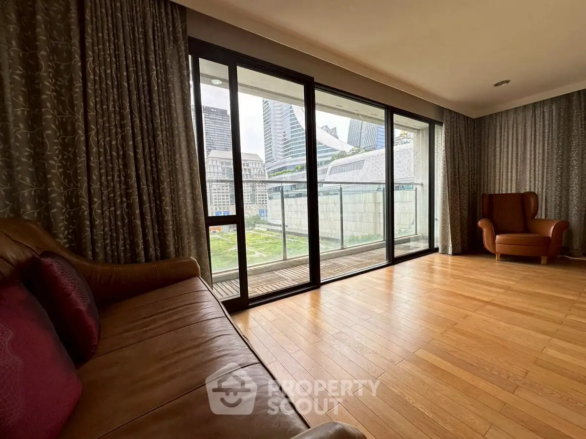 Spacious living room with floor-to-ceiling windows and city view, featuring elegant hardwood flooring.