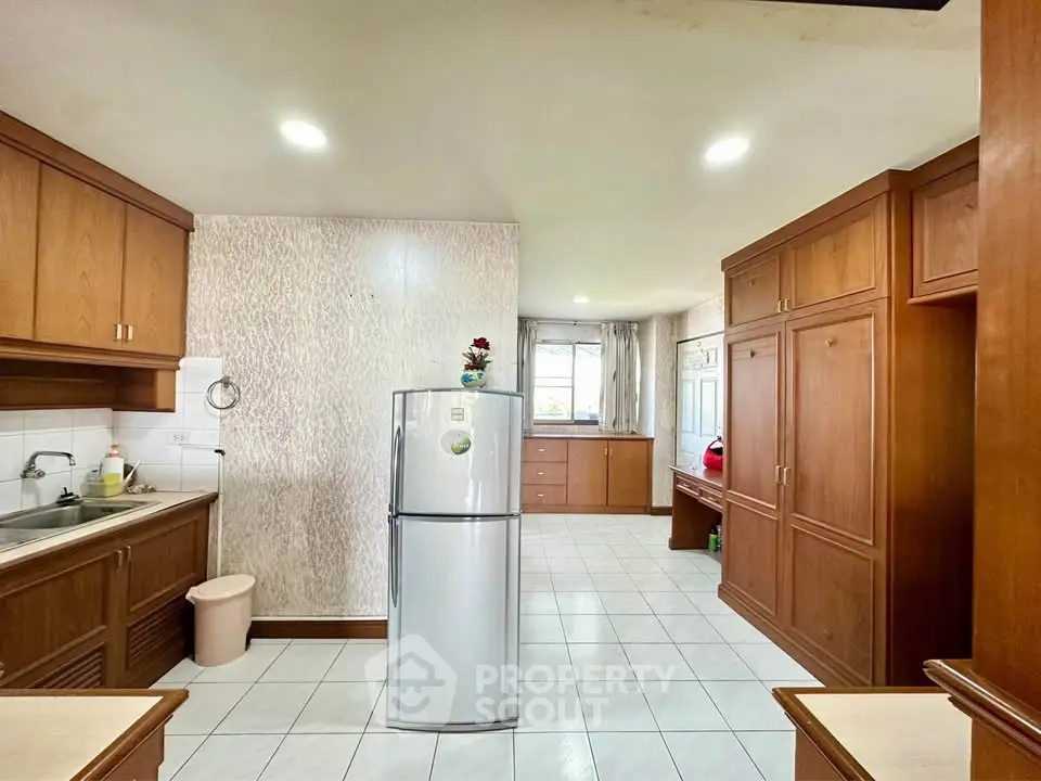 Spacious kitchen with wooden cabinets and modern fridge in a bright, tiled room.