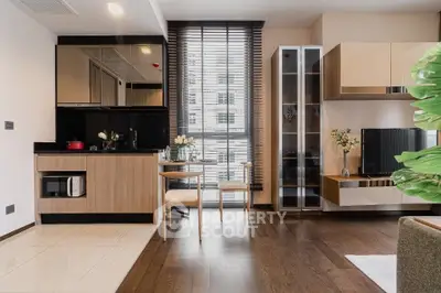 Modern living room with open kitchen, stylish decor, and large window offering natural light.