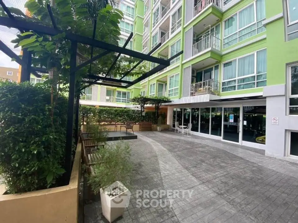 Modern apartment building exterior with green facade and spacious entrance area.