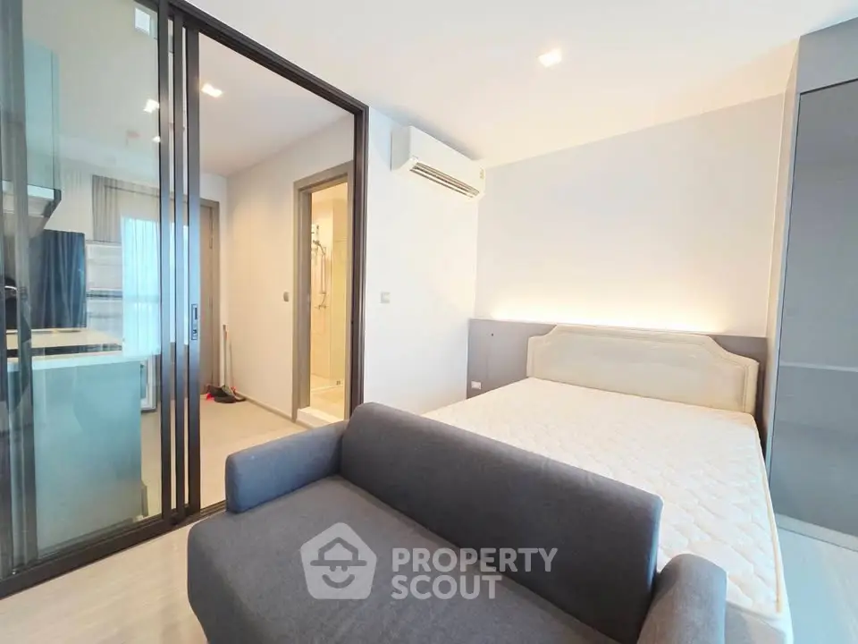 Modern studio apartment with open layout, featuring a cozy bed and sleek glass partition for kitchen area.