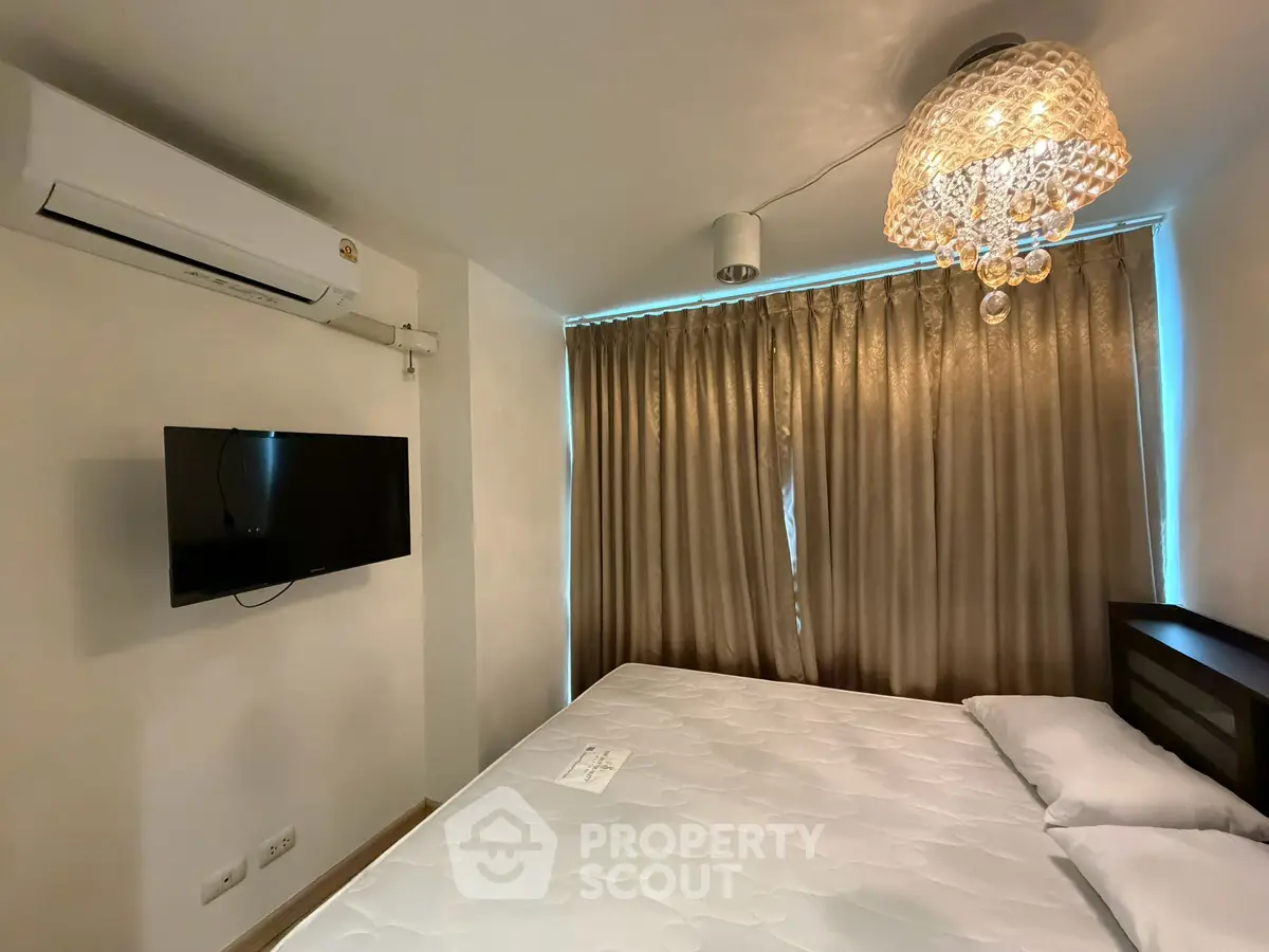 Modern bedroom with elegant chandelier and wall-mounted TV, featuring a comfortable bed and air conditioning.