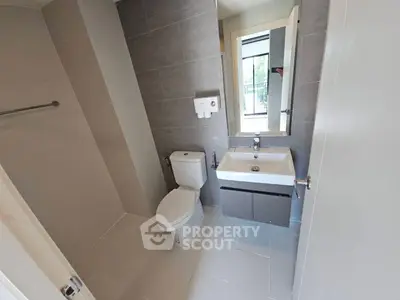 Modern bathroom with sleek fixtures and neutral tiles, featuring a large mirror and window view.