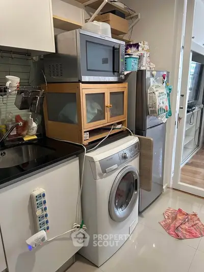 Compact kitchen with washing machine, microwave, and fridge in modern apartment.