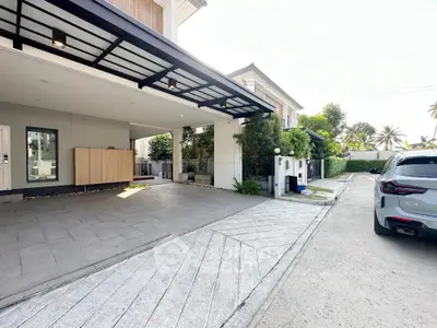 Modern house exterior with spacious driveway and carport, surrounded by lush greenery.