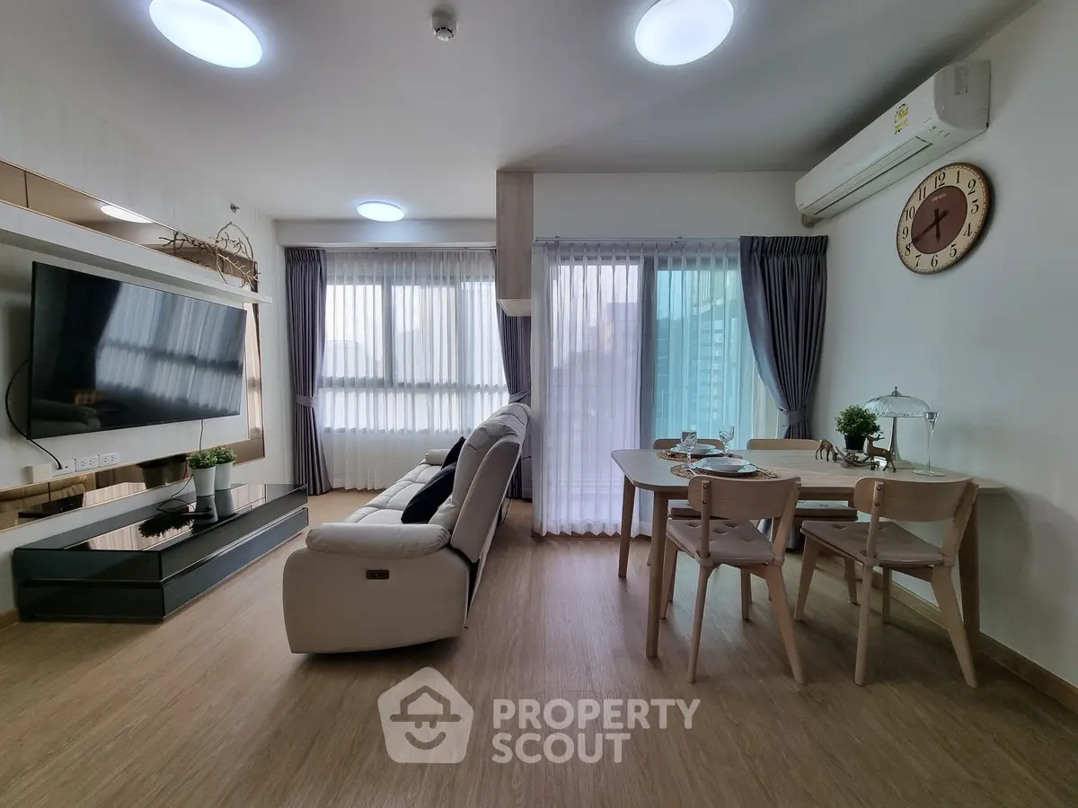 Modern living room with stylish furniture and natural light, featuring a cozy dining area and large TV.