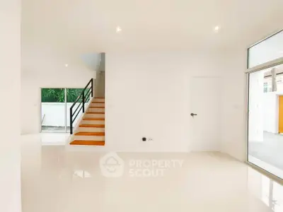 Spacious modern living room with sleek staircase and large windows for natural light.