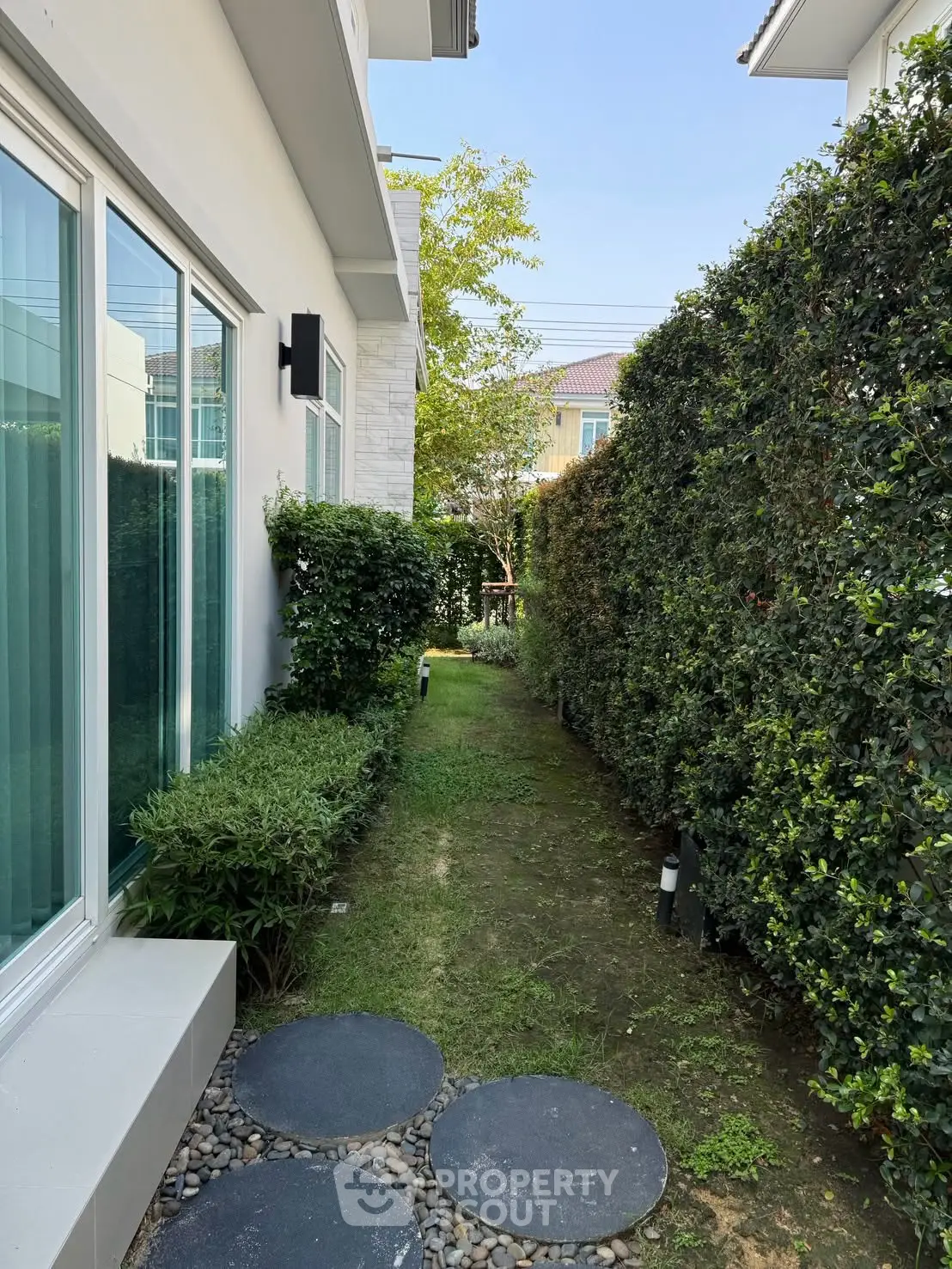 Charming garden pathway beside modern home with lush greenery and stepping stones.