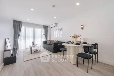 Modern living room with stylish decor and open dining area, featuring large windows and elegant furnishings.