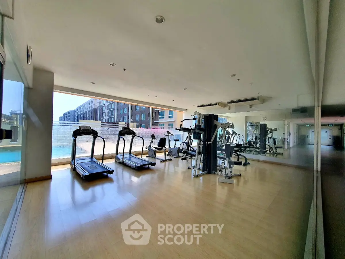 Spacious gym with modern equipment and pool view in luxury apartment complex.