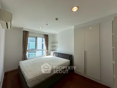 Spacious bedroom with large window and modern furnishings in a bright apartment.
