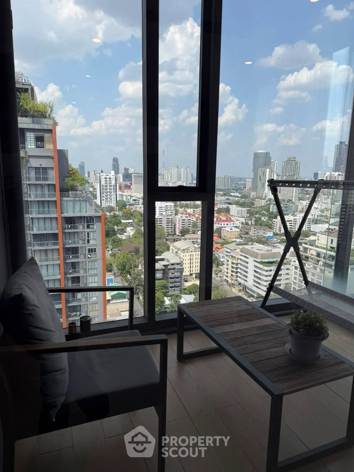 Stunning city view from modern high-rise balcony with cozy seating area.