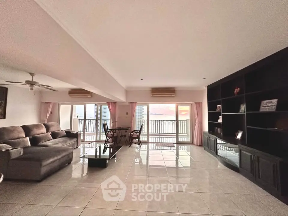 Spacious living room with large windows and sunset view, featuring modern furniture and tiled flooring.