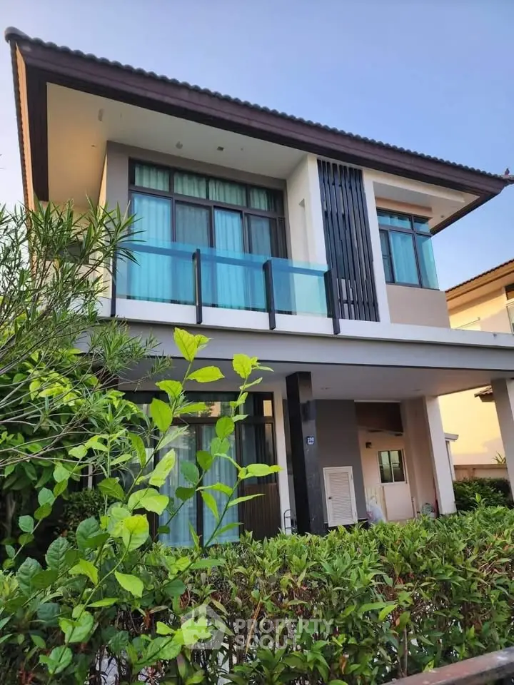 Modern two-story house with large windows and lush greenery in a serene neighborhood.
