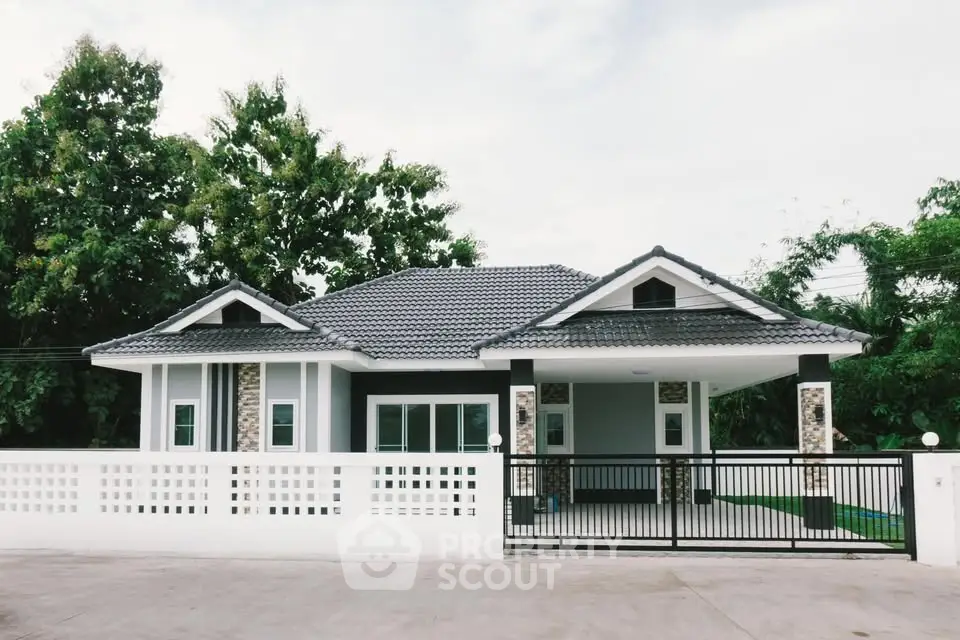 Charming modern house with stylish roof and gated entrance, surrounded by lush greenery.