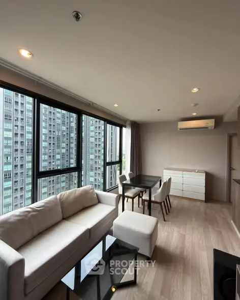 Modern living room with large windows and city view, featuring a cozy sofa and dining area.