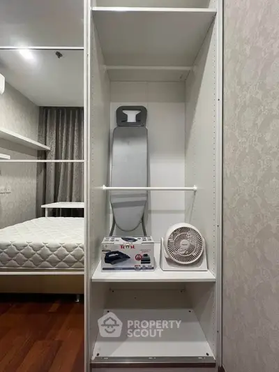 Spacious bedroom with built-in closet featuring ironing board and fan, perfect for modern living.