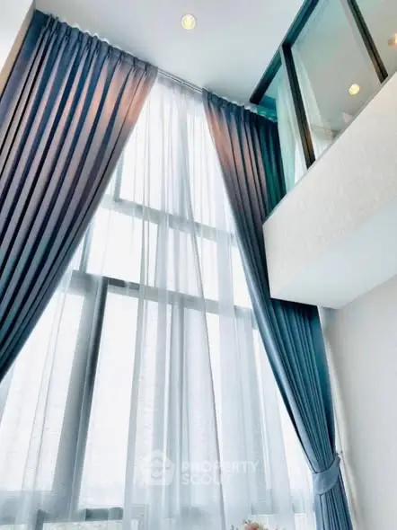 Elegant high-ceiling living room with floor-to-ceiling windows and blue curtains