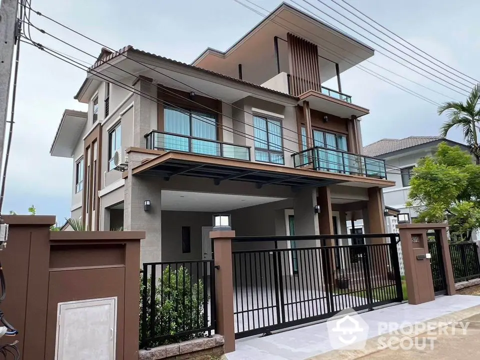 Modern two-story house with spacious balcony and gated entrance in suburban neighborhood.