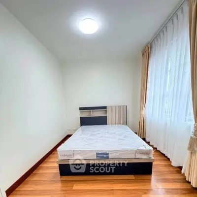 Cozy bedroom with wooden flooring and natural light through large window.