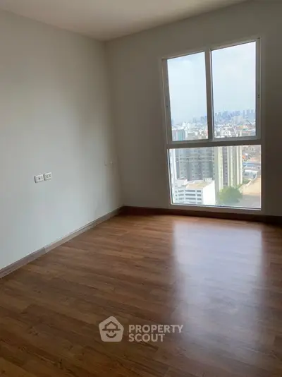 Bright empty room with wooden flooring and city view from large window.