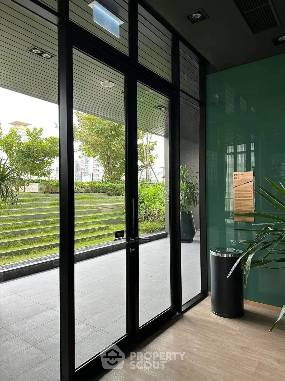 Modern building entrance with glass doors and lush greenery outside