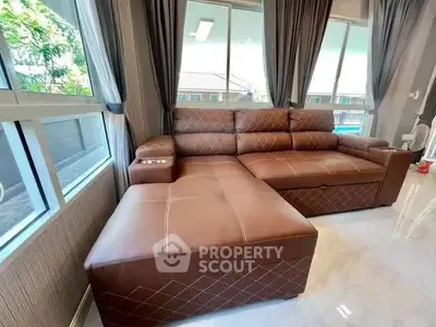 Spacious living room with luxurious brown leather sectional sofa and large windows offering natural light.