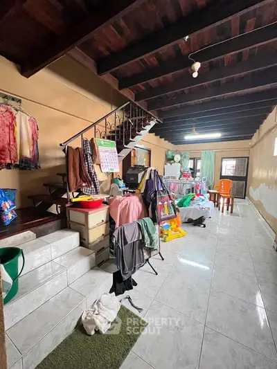 Spacious living area with wooden ceiling and tiled floor, featuring a staircase and ample natural light.
