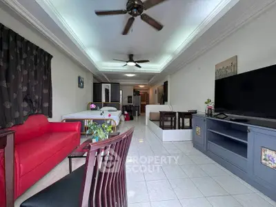 Spacious living room with modern decor and ceiling fans, featuring a red sofa and large flat-screen TV.
