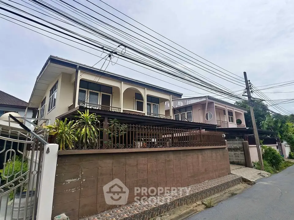 Charming two-story house with spacious balcony and lush greenery in a serene neighborhood.