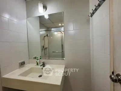 Modern bathroom with sleek white tiles and a spacious mirror, featuring a contemporary sink and shower area.