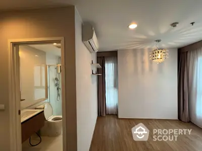 Spacious and well-lit corner unit with elegant chandelier, large windows with curtains, and a peek into the modern bathroom.