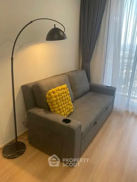 Cozy living room with modern gray sofa, stylish floor lamp, and large window with curtains.