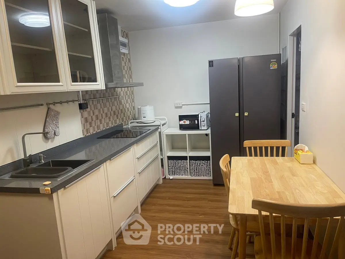 Modern kitchen with sleek cabinets, dining table, and appliances in a cozy setting.