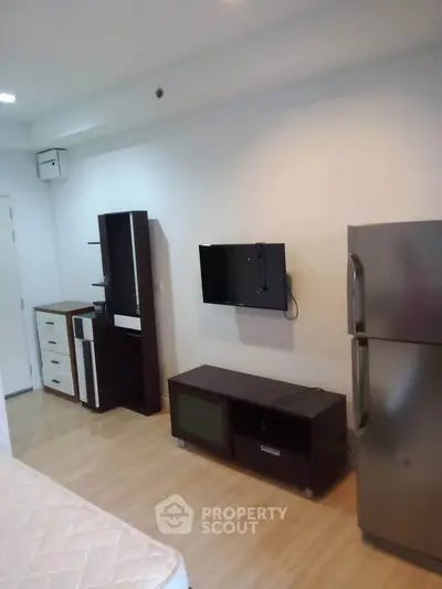 Modern studio apartment with sleek furniture and mounted TV, featuring a spacious fridge and wooden flooring.